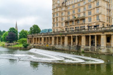 BATH, İngiltere - 27 Haziran 2021: Weir ve Bath 'daki Avon Nehri' nin manzarası, Somerset 'in en büyük şehri, Roma' nın inşa ettiği hamamların adı ve adı ile bilinir..