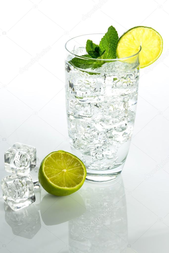Glass of sparkling water with ice cubes on white background
