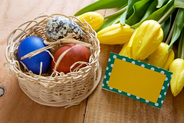 Easter basket with colored eggs and yellow tulips. — Stock Photo, Image