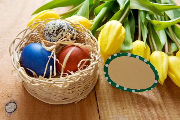 Easter basket with colored eggs and yellow tulips. — Stock Photo, Image