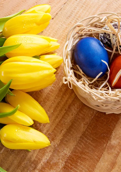 Великодній кошик з кольоровими яйцями і жовтими тюльпанами . — стокове фото