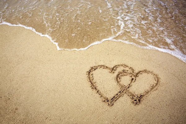 Zwei Herzen auf dem Sand eines Strandes gezeichnet. — Stockfoto