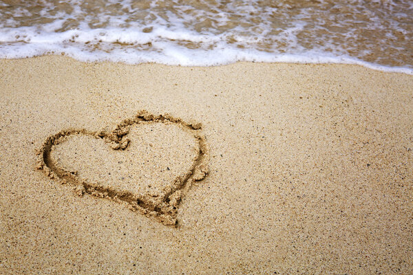 Heart symbol on the sand and sea wave.