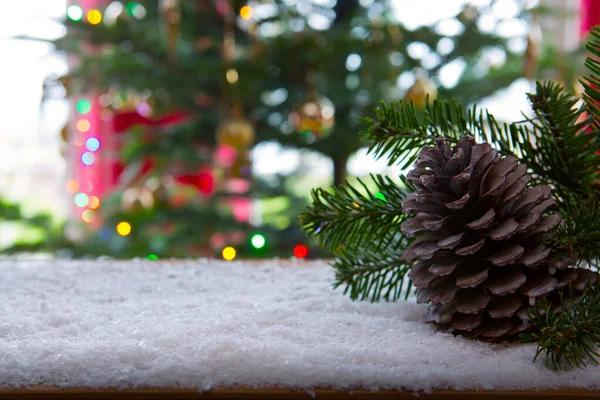 Cone de abeto na neve branca isolada no borrão luzes da árvore de Natal fundo. — Fotografia de Stock