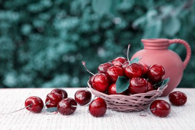 Sepette büyük kırmızı kirazlar ve yeşil üzerine izole edilmiş bir sürahi süt..