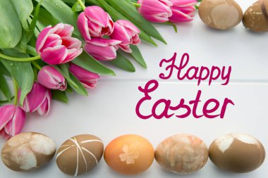 Beyaz ahşap üzerinde pembe laleler ve renkli yumurtalarla dolu Paskalya kartı. .