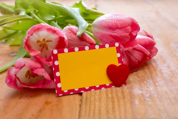 Różowe tulipany kartą serca na tle drewna. — Zdjęcie stockowe