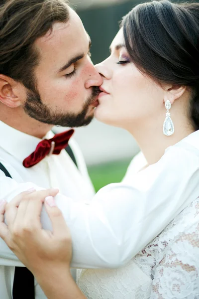 Braut und Bräutigam küssen sich. Hochzeitspaar, Brautpaar küssen sich. Porträt schließen. der Mann mit Fliege und Hosenträgern. — Stockfoto