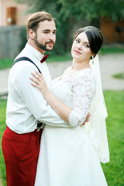 时尚夫妇站拥抱，寻找到一侧。新郎与胡须、 胡子、 蝴蝶领带和吊带。穿着白色婚纱的新娘. — 图库照片