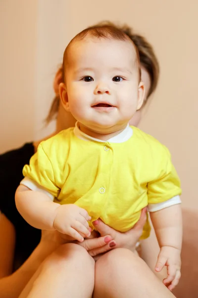 Happy cheerful kid in yellow shirt, portrait. Looking straight into camera, standing with support of mother at background. — Stock Photo, Image