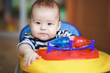 Portre ciddi sert bebek bir oyuncak arabanın direksiyonuna.