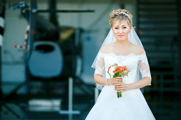 Bride with wedding bouquet on background of helicopter in hangar — Stock Photo, Image