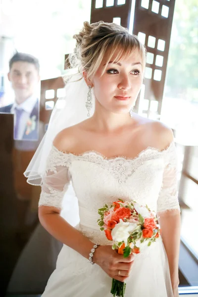 Menyasszony a vőlegény mögött üveg, menyasszonyi csokor, kezében beltéri gyönyörű portréja. — Stock Fotó