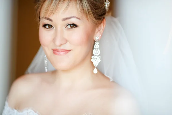 Primer plano retrato de la novia sonriente sobre fondo naranja con velo y pendientes en vestido de novia . Fotos De Stock Sin Royalties Gratis