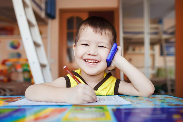 Niño feliz hablando en el teléfono inteligente en casa mientras escribe cartas . —  Fotos de Stock