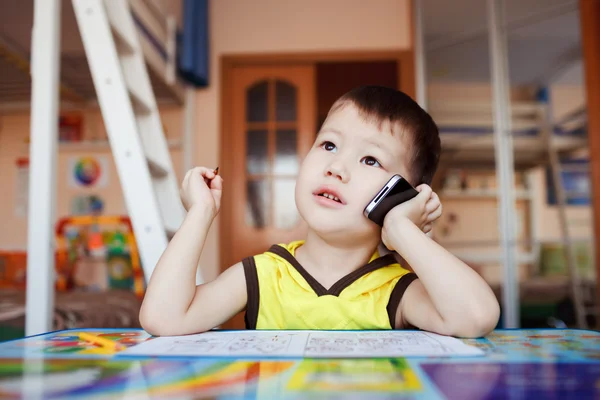 Kleine jongen neemt een belangrijke oproep op zijn mobiele telefoon, terwijl thuis tekenen met pennen voelde. — Stockfoto