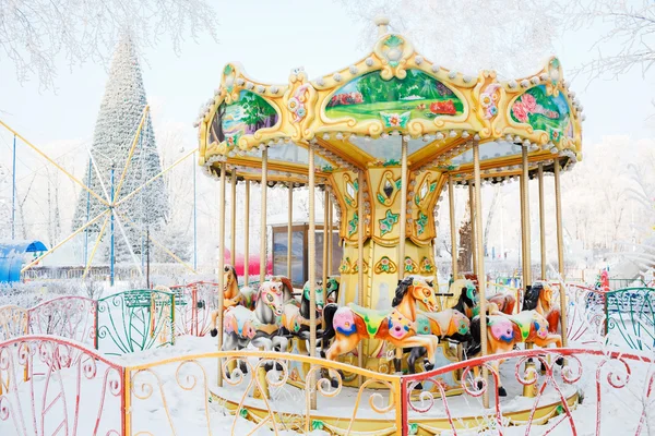 Merry-go-round traditional horses covered with snow. Behind the carousel big Christmas tree. — Stock Photo, Image