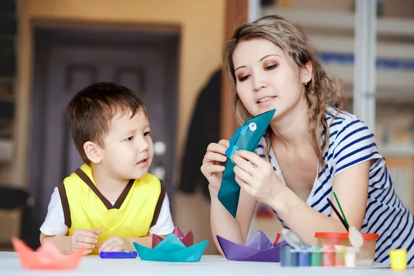 Curiosa infancia, un niño jugando con su madre, dibuja, pinta en las palmas de las manos. Enseñar a los niños dibujo, desarrollo de habilidades creativas. Haciendo monstruos y barcos de origami . — Foto de Stock