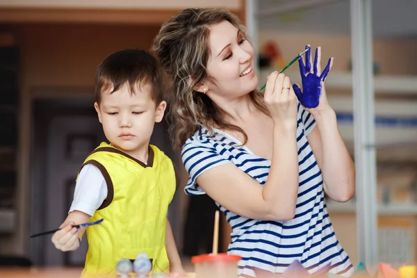 Feliz infância, um menino brincando com sua mãe, desenha, pinta nas palmas das mãos. Ensinando crianças desenho, desenvolvimento de habilidades criativas. Luz natural do dia . — Fotografia de Stock