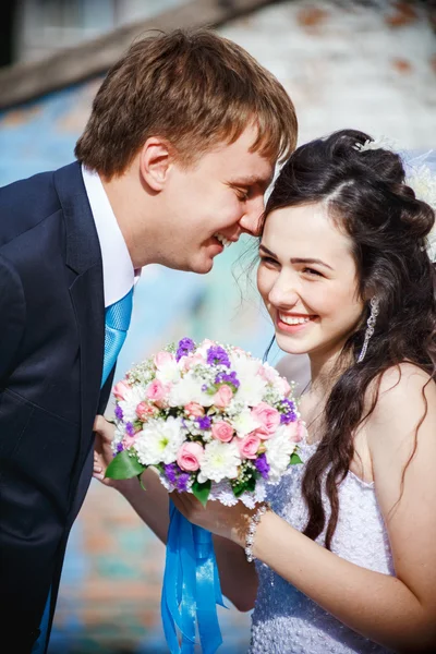 Les mariés sont roulés de rire, de rire, de rire joyeusement. Portant une cravate turquoise, il se pencha sur sa femme portant une robe de mariée blanche, tenant un bouquet. Jeunes mariés, plan vertical . — Photo