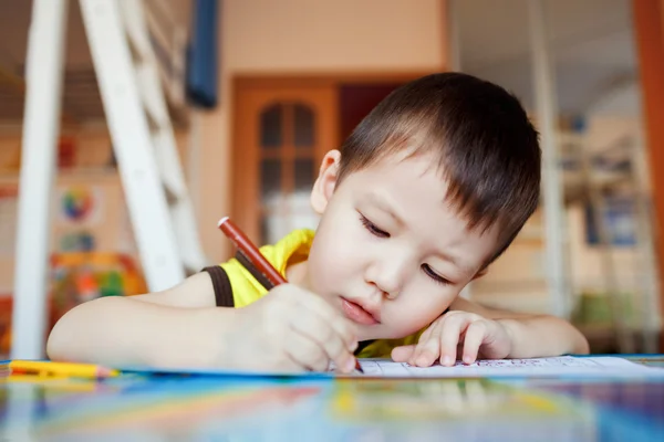 Мальчик тщательно и целенаправленно рисует специальный блокнот для рисования, обучения дома, дошкольного воспитания, развития творческих способностей детей. Класс . — стоковое фото