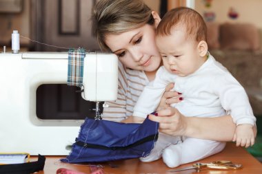 Onun annesi terzi bebekle, ev, doğal ışık, Bebek merakla dikiş makinesi için arıyorum. Çocuk Bakımı ve iş evde.