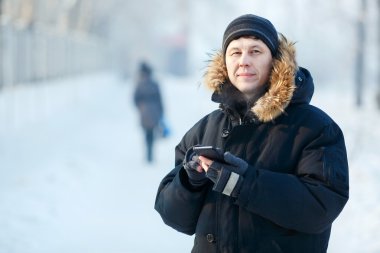 Ceket, kürk başlık aşağı sıcak giyen genç bir Sibirya adam elinde, telefon ile portresi. Soğuk kış günü, iletişim, her türlü hava, kar, frost. Mesafe içine arıyorum. Metniniz için yer.
