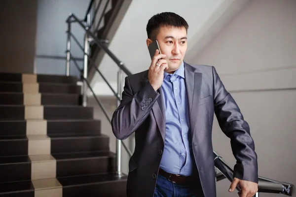 Geschäftsmann mit Telefon in der Hand telefoniert in der Pause auf der Treppe eines Bürogebäudes im Anzug. Geschäftsporträt eines männlichen mittelasiatischen Aussehens. — Stockfoto