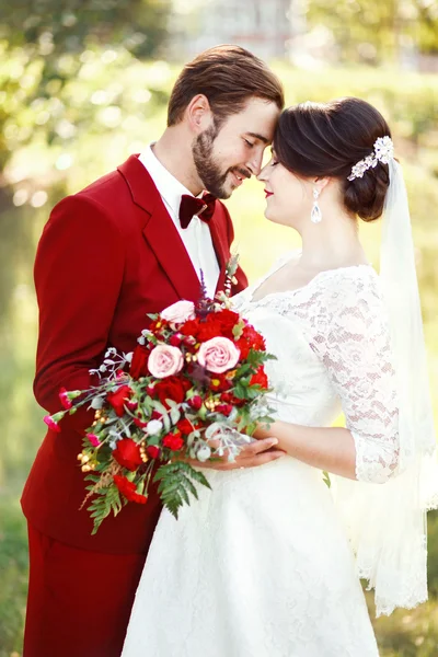 Bruid en bruidegom omarmen, bruidspaar, donkerrood marsala stijl ontwerp. Pak met kastanjebruine strikje, witte jurk, bruids boeket. Professionele make-up. Eeuwige liefde, tederheid, schoonheid concept. — Stockfoto