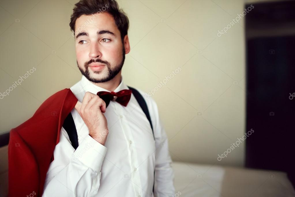 Stylish groom in tuxedo suit marsala red, burgundy bow tie, professional  hairstyle, beard, mustache. Wedding preparations, getting ready. Man  holding jacket over shoulder. Copy space for text. Stock Photo by  ©maynagashev 97796912