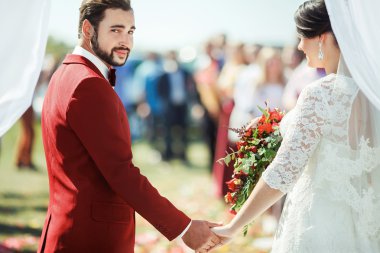 Damat Düğün töreni Arch gelinler elle kalabalık arka plan üzerinde dururken kamera anlamlı bakıyor. Yeni yaşam konsepti.