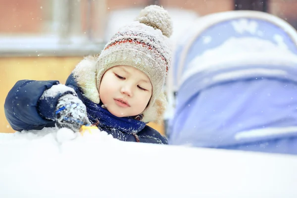 Liten pojke spela ensam med leksaken i snö, på nära håll. Utanför, vinter. — Stockfoto