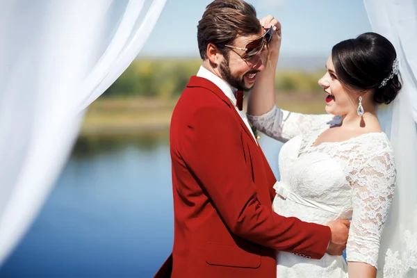 Bruid en bruidegom gek rond op foto schieten na de ceremonie, binnen boog met witte doeken stof. Bruiloft kleur Marsala. — Stockfoto