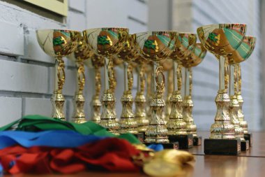 Altın madalyalar, renkli kurdeleler ve altın kupalar kazananlar için ahşap bir masada.