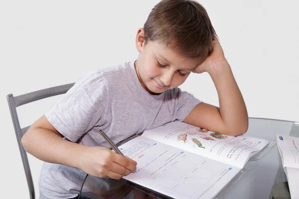 Boy does his homework on a glass table — Stock Photo, Image