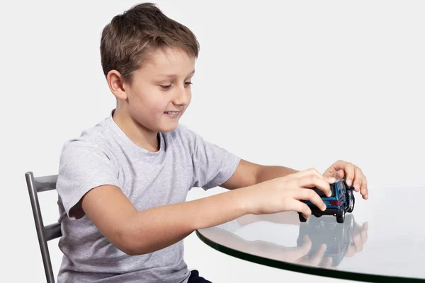 Мальчик играет с синей машиной на стеклянном столе — стоковое фото