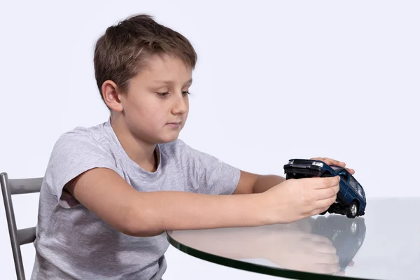 Boy playing with blue car on a glass table — Stock Photo, Image