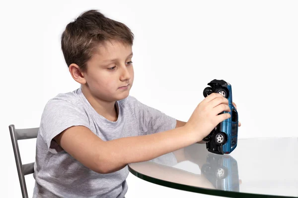 Мальчик играет с синей машиной на стеклянном столе — стоковое фото