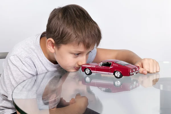 Boy playing with red sports car on a glass table — Stock Photo, Image