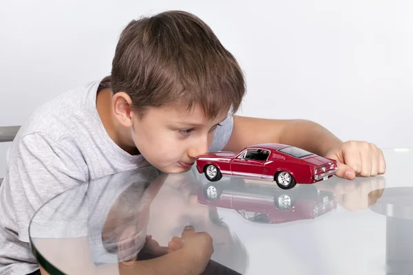 Garçon jouant avec voiture de sport rouge sur une table en verre Photos De Stock Libres De Droits