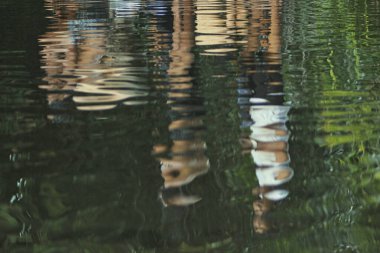 Nehirde yıkanmaya giden insanların aktiviteleri suyun yansımasında görülüyor.