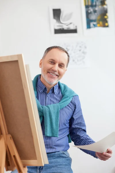 Cheerful senior painter is drawing the image — Stock fotografie
