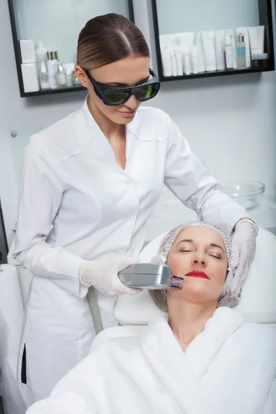 Fröhliche Kosmetikerin macht Lasertherapie in Klinik — Stockfoto