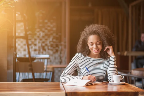 Cheerful young woman is writing in notebook — Stock Photo, Image