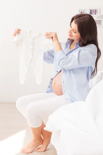 Hermosa madre embarazada está mostrando ropa pequeña —  Fotos de Stock