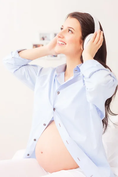 かなり妊娠中の母親は音楽を聴いている — ストック写真