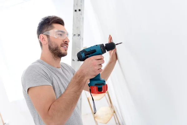 Young guy drilling white wall — Stok fotoğraf