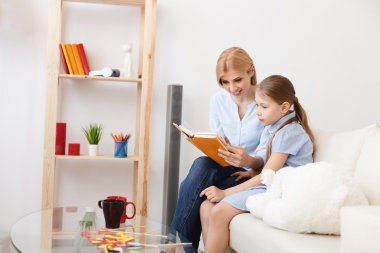Anne ve kızı evde kitap okuyorlar.