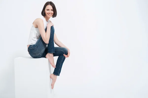 Schöne junge Frau sitzt auf White Cube im Studio — Stockfoto