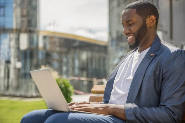 Vrolijke Afrikaanse man met computer buitenshuis — Stockfoto